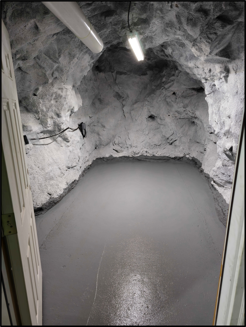 Interior of CURIE site 1 in the Edgar Experimental Mine. Interior of a rock-walled cave illuminated by overhead tube lights.